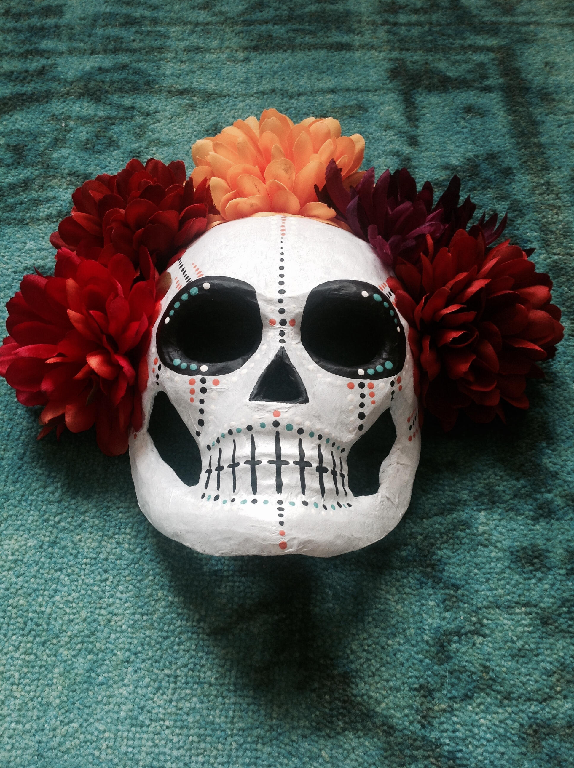 Paper-mâché skull mask decorated with colorful painted dots and crowned with large autumn-colored flowers